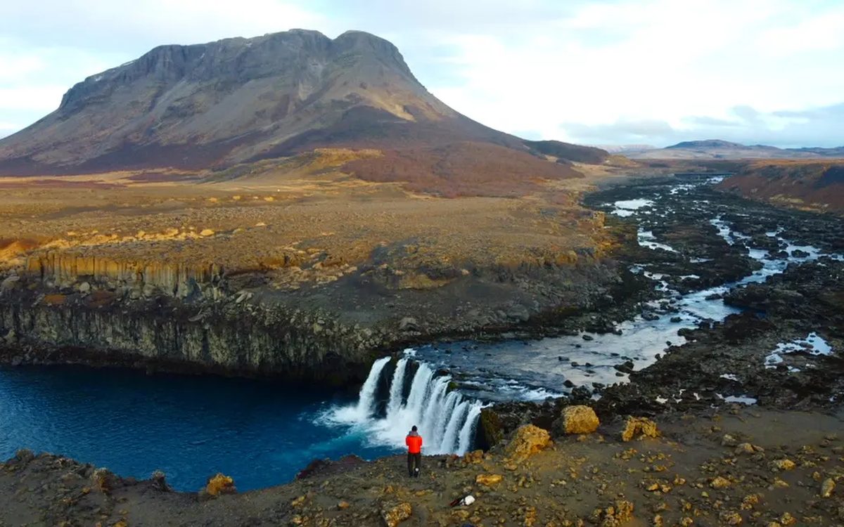 A photographer beside a waterfall beneath a mountain in Iceland